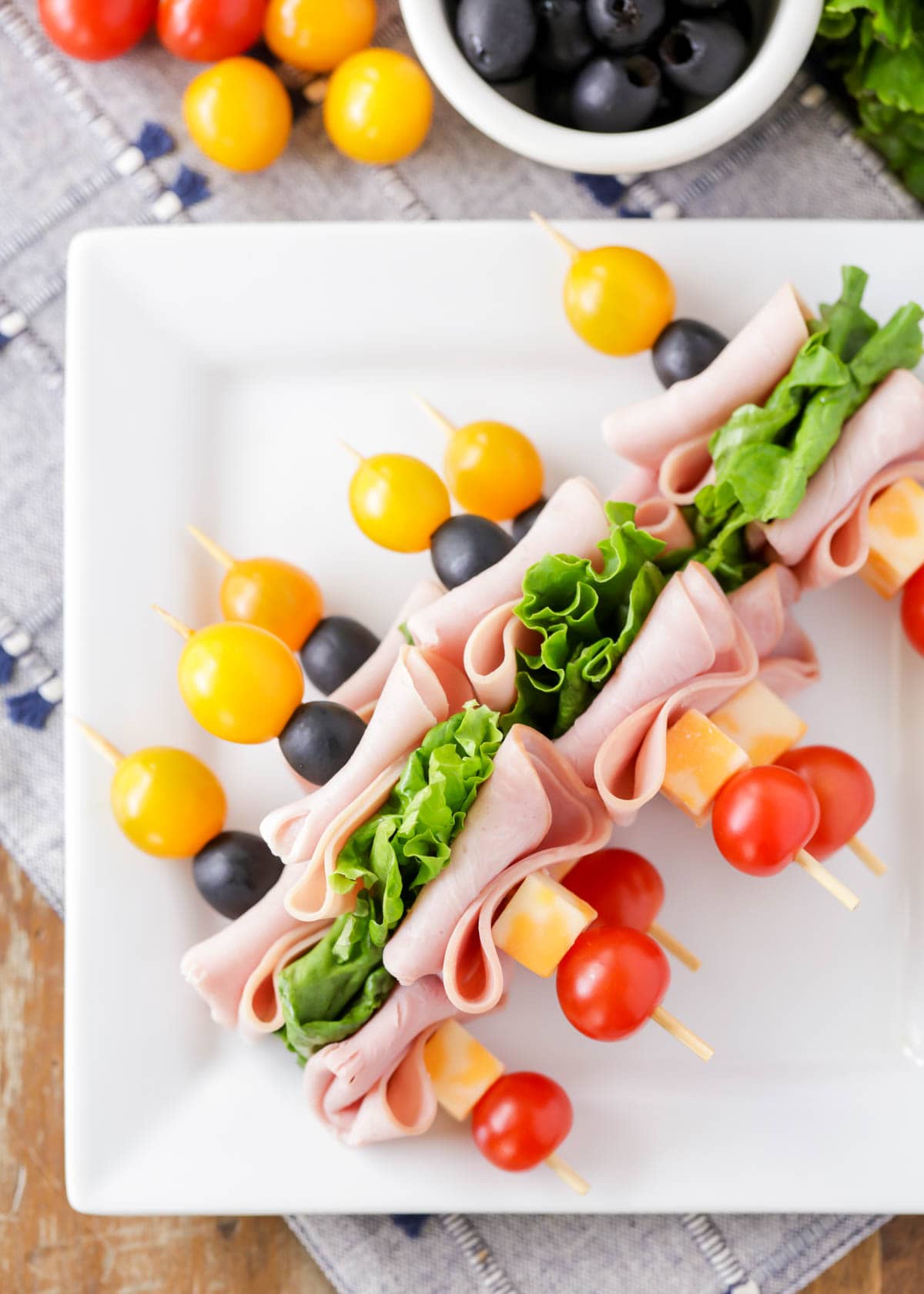 Deli meat kabobs with cheese, tomatoes, olives, and lettuce on a white plate